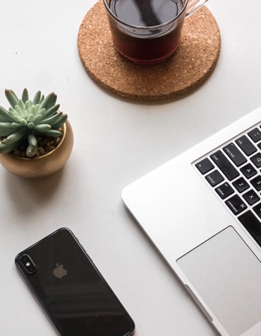 A desk with an IPhone, a succulent, a cup of coffee and half a macbook.